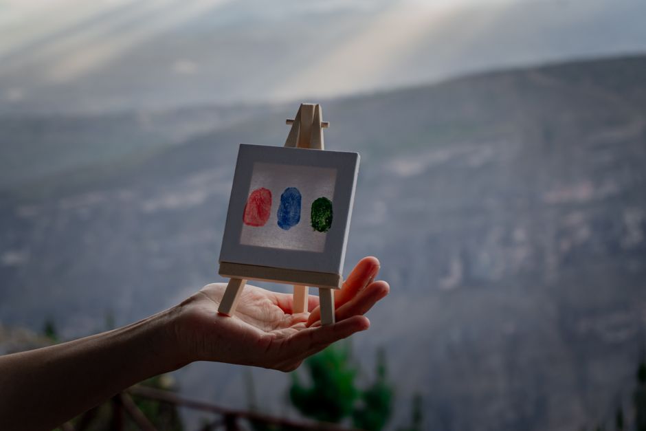 A human hand with a paintbrush adding vibrant, custom details to a canvas where an AI has generated a complex, but generic, base artwork, symbolizing human refinement.