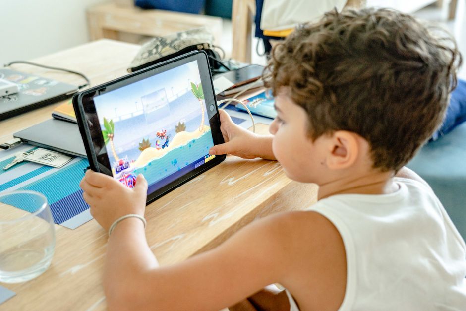 Two children, a boy and a girl, sitting together and focused on a tablet displaying a game with French text elements, suggesting language learning through play.