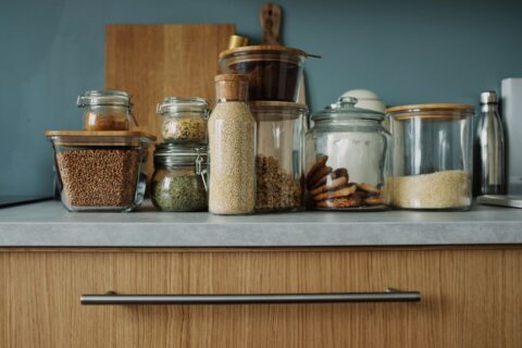 A clean kitchen counter filled with various glass meal prep containers, some filled with prepped vegetables, cooked grains, and protein, illustrating organized batch cooking.