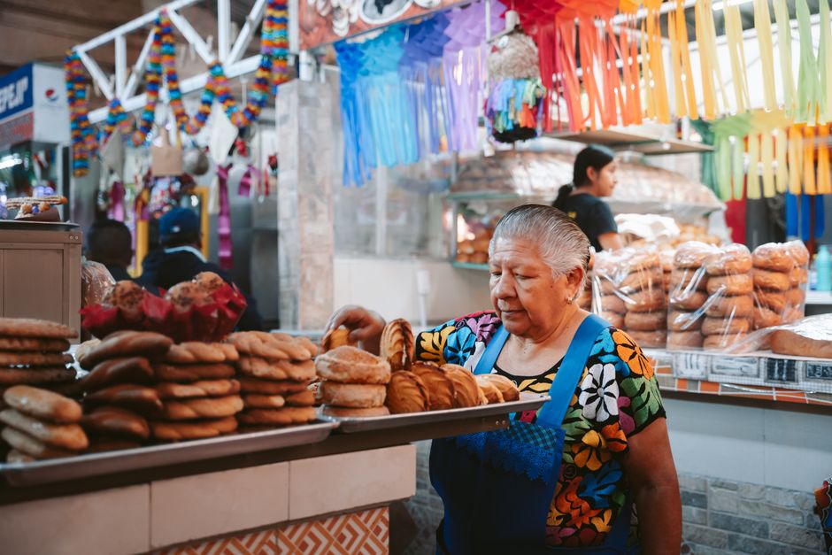 A vibrant street scene in a Latin American city, featuring people in colorful clothing, patterned dresses, and large accessories, showcasing street style.