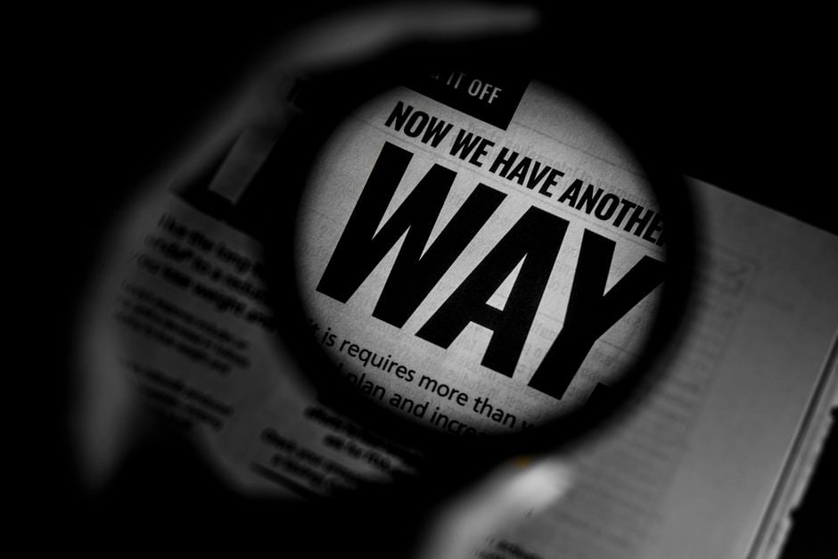 A hand holding a magnifying glass over a tablet displaying AI-generated text, highlighting the critical examination of AI output.