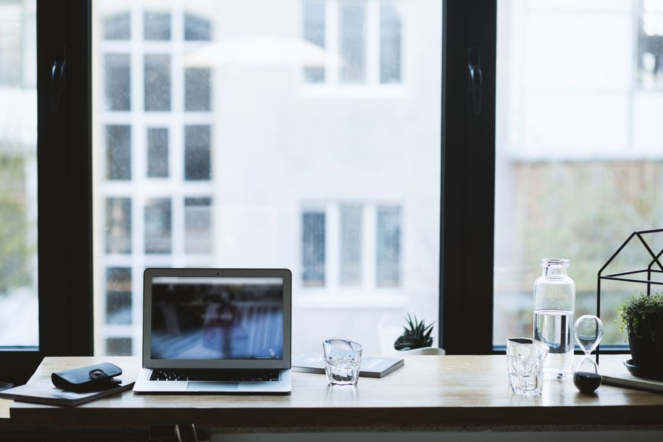 A clean, minimalist home office space with a wooden desk, a laptop, a plant, and a comfortable chair, bathed in natural light.