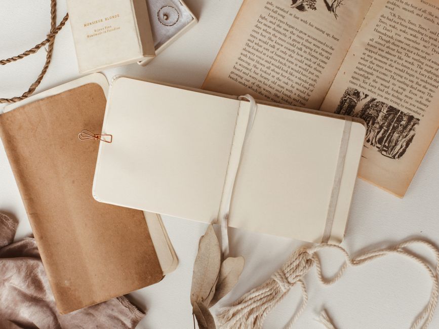 An open travel journal lies on a rock overlooking a stunning panoramic view of mountains and a serene lake at sunset, with a pen resting on its pages, symbolizing reflection amidst natural beauty.