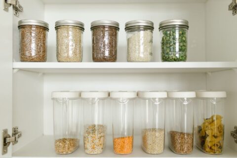 A neatly organized kitchen pantry stocked with olive oils, canned goods, whole grains, and dried herbs, ready for Mediterranean cooking.