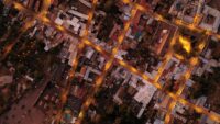 An aerial view of a sprawling modern city at night, with illuminated roads and dense buildings, showcasing complex urban infrastructure.