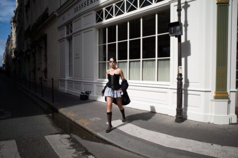 A stylish Parisian woman walking on a city street, wearing a beige trench coat, tailored trousers, and ballet flats, embodying Parisian minimalism.