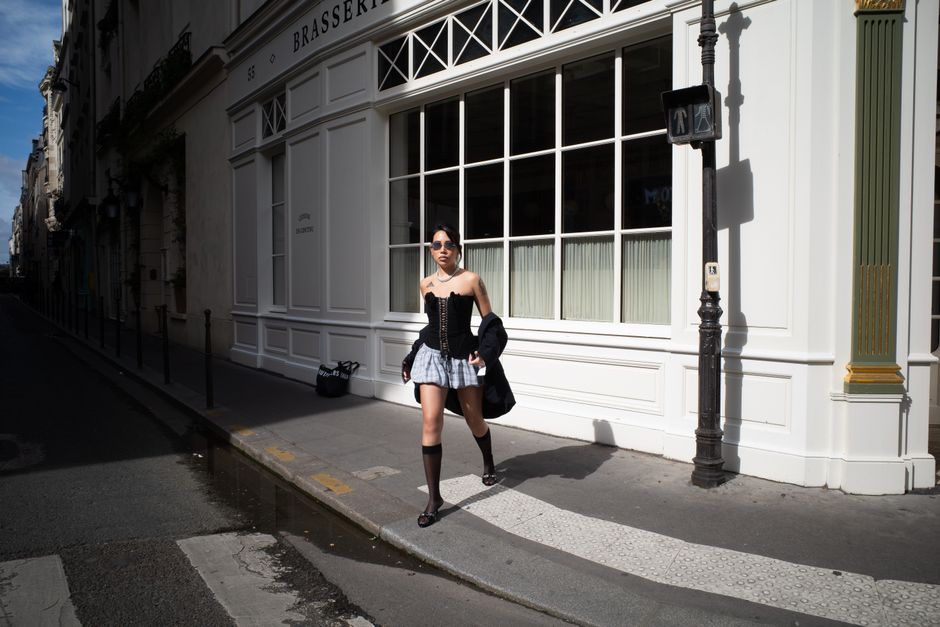 A stylish Parisian woman walking on a city street, wearing a beige trench coat, tailored trousers, and ballet flats, embodying Parisian minimalism.