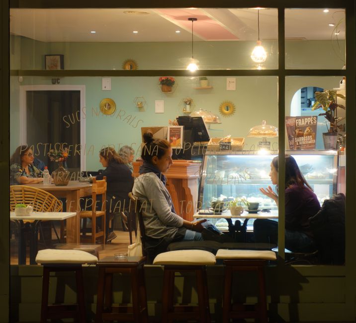 People sitting at outdoor tables, enjoying coffee and conversation in front of a small, inviting independent cafe in a walkable urban neighborhood.