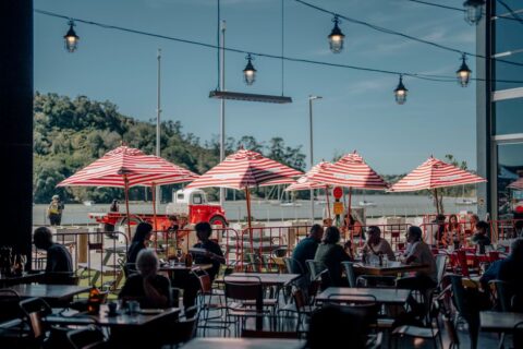 A group of diverse people laughing and eating together at an outdoor cafe table, with vibrant food and drinks, symbolizing a leisurely European lunch.