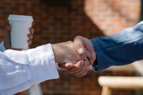 Two business people shaking hands over a table, signifying agreement and trust after a successful interaction.