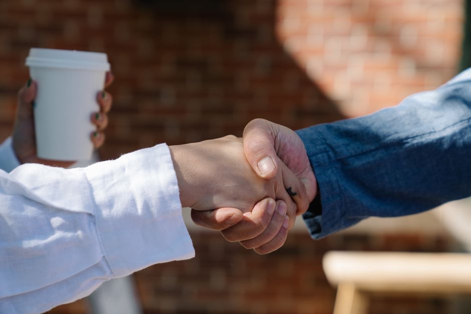 Two business people shaking hands over a table, signifying agreement and trust after a successful interaction.