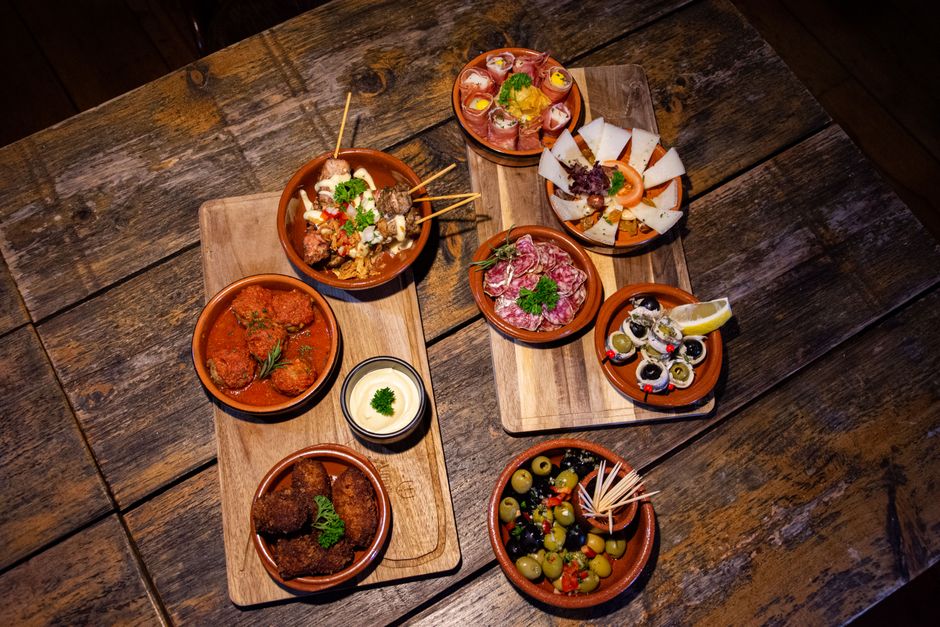 Friends sharing various small plates and drinks at a lively outdoor tapas bar, showcasing a communal and balanced dining experience.