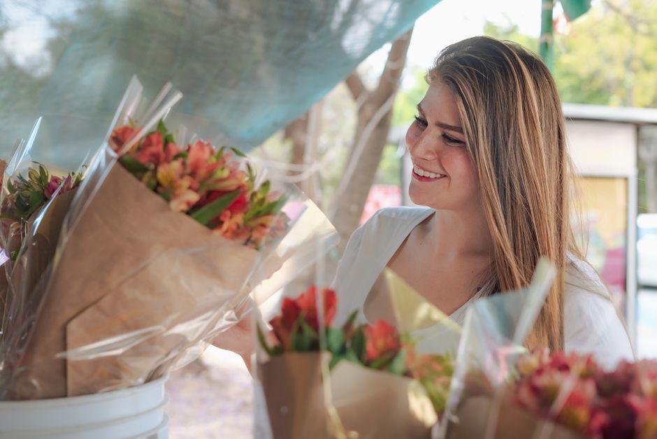 A person paying for flowers at a vibrant market stall, showcasing a practical crossbody bag and comfortable footwear perfect for weekend market outfits.