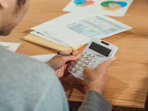 A person with glasses meticulously reviewing financial spreadsheets and charts on a desk, representing budget planning for a small online brand.
