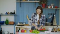 A person happily cooking a colorful, healthy meal in a bright kitchen, symbolizing home cooking as a low-spend strategy.