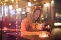 A person sips coffee while working on a laptop in a warmly lit, comfortable neighborhood cafe, embodying a calm travel anchor experience.