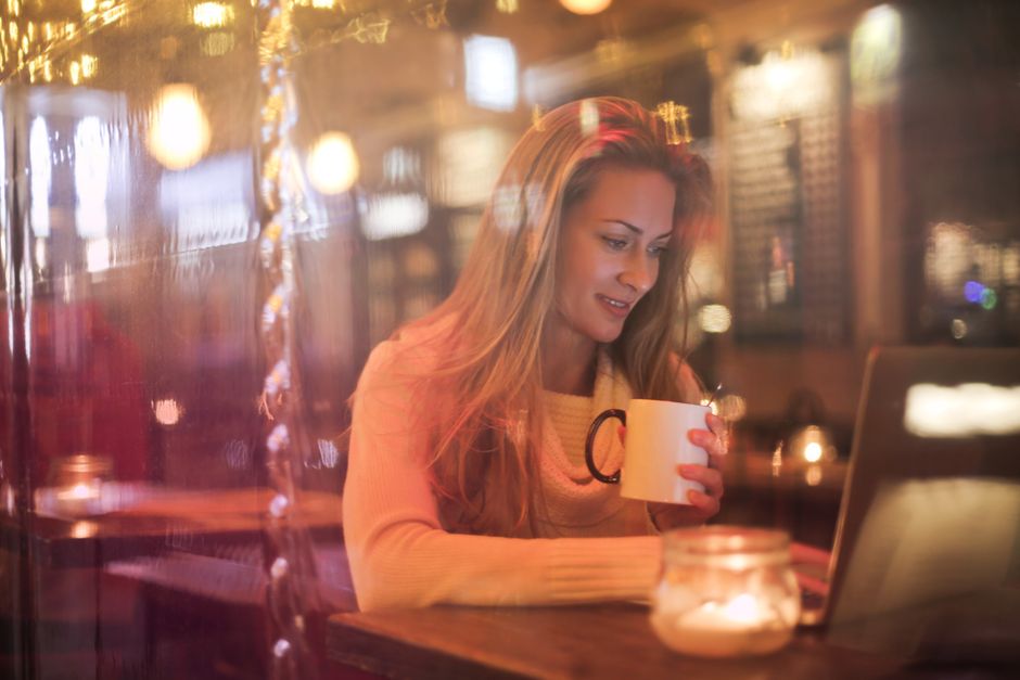A person sips coffee while working on a laptop in a warmly lit, comfortable neighborhood cafe, embodying a calm travel anchor experience.