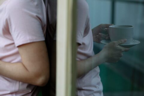A person sips coffee in a sunlit living room, looking calm and relaxed, symbolizing a peaceful start to a Sunday.