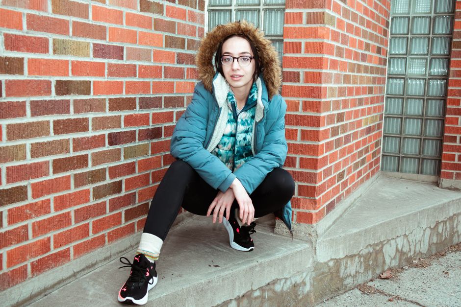 Stylish individual on a city street, dressed in layered technical and natural fabrics, suitable for changing urban weather conditions.