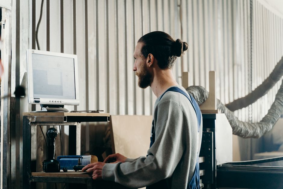 A person intently focused on a computer screen, designing complex production lines and logistics in a factory building game with a clear interface.