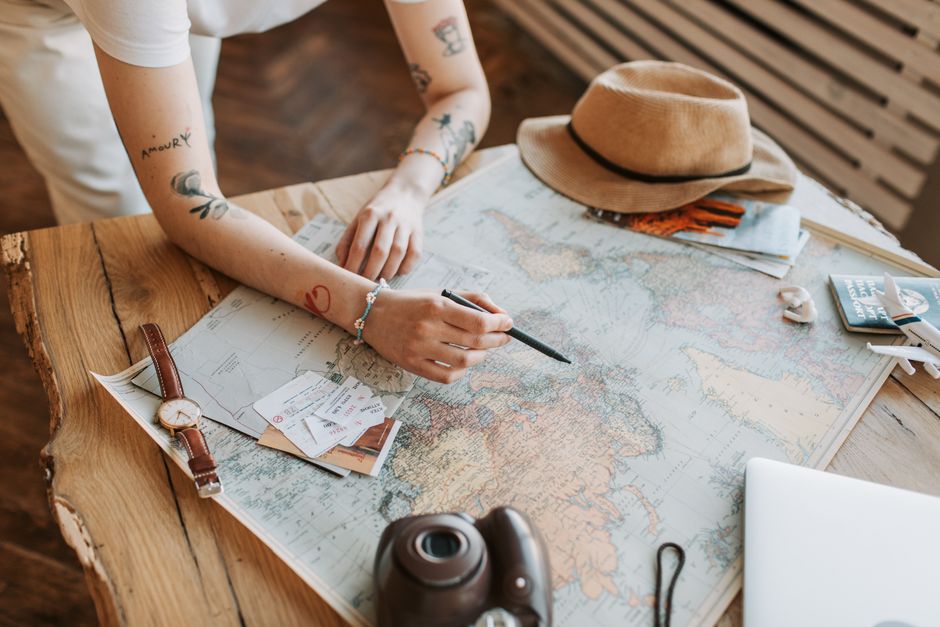 A close-up of a person's hands studying a paper map while also looking at a laptop, illustrating strategic travel planning.