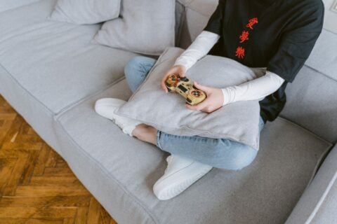 A student relaxing on a sofa, happily playing a serene-looking game on a console, illustrating how to choose calm games for evenings.