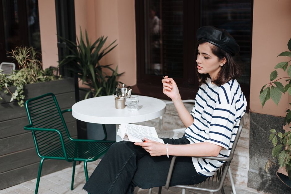 A person engrossed in a book at a small table outside a classic Parisian café, with blurred street life in the background, illustrating a literary city break.