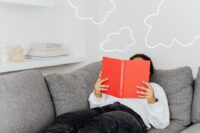A person comfortably reading a book on a sofa, surrounded by blankets and soft lighting, symbolizing the reader's love for stories.