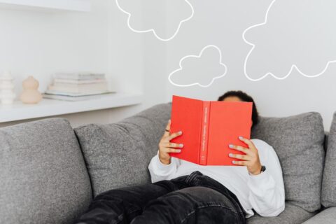 A person comfortably reading a book on a sofa, surrounded by blankets and soft lighting, symbolizing the reader's love for stories.