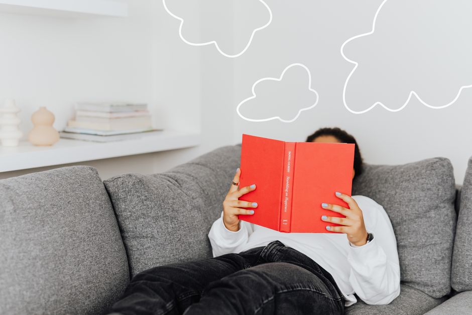 A person comfortably reading a book on a sofa, surrounded by blankets and soft lighting, symbolizing the reader's love for stories.
