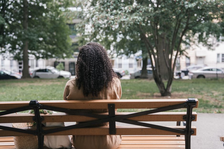 A serene person sitting on a bench in a vibrant city park, looking contemplative, with the blurred skyline of a European city in the background, illustrating white space and relaxation.