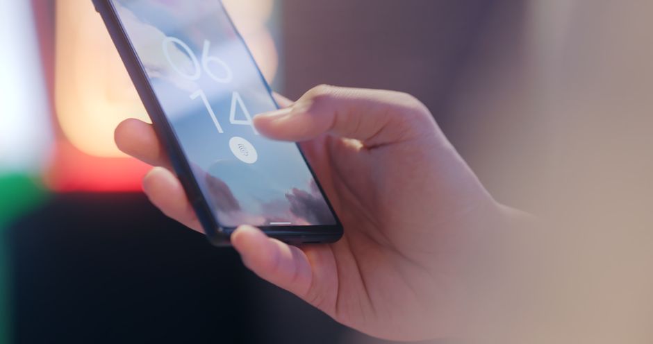 A close-up shot of a hand pressing a thumb onto a smartphone screen, which displays a fingerprint icon, illustrating biometric authentication for passkeys.