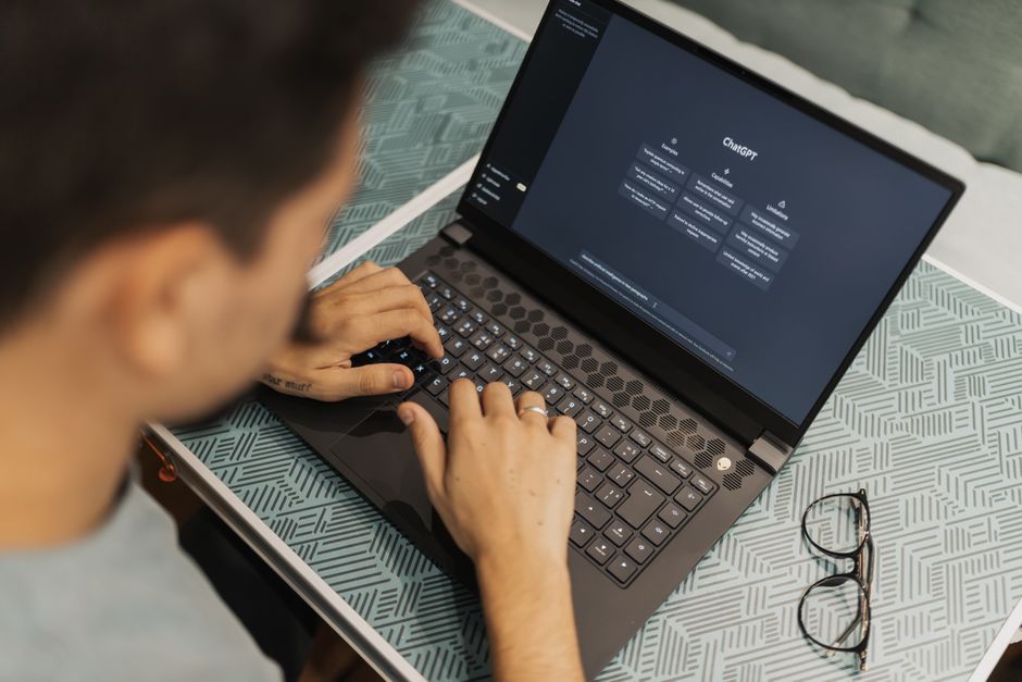 Close-up of a hand pointing at a tablet screen displaying different AI software features and comparison tables, with a blurred background of a modern office or university setting.