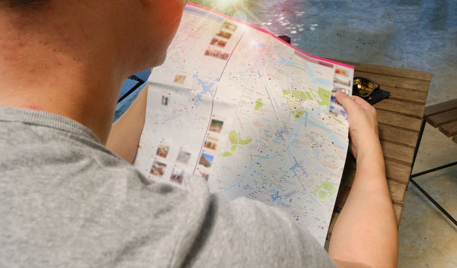 A person with a backpack consulting a physical map while standing on a charming European street, looking thoughtful and ready to explore their new neighborhood.