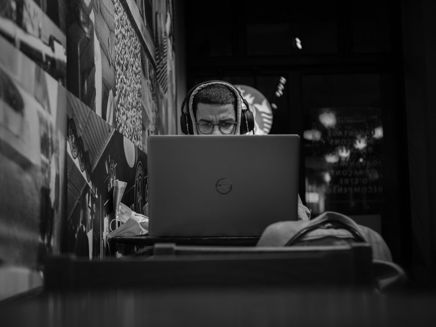 A remote worker in a bustling cafe, focused on their laptop while wearing large, over-ear noise-cancelling headphones.