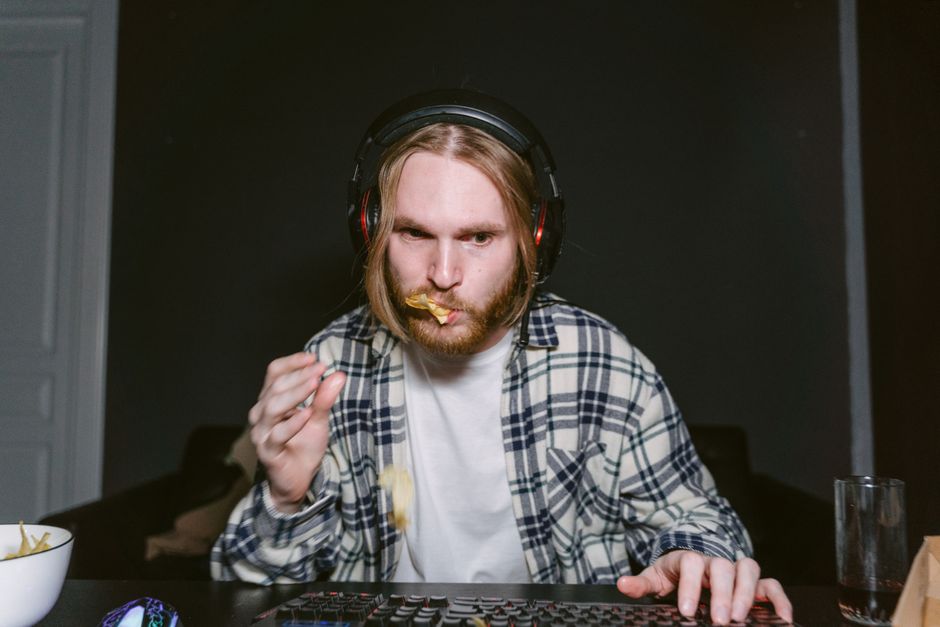 A person at a desk late at night, reaching for a bowl of fruit and nuts instead of unhealthy snacks, with a laptop open.