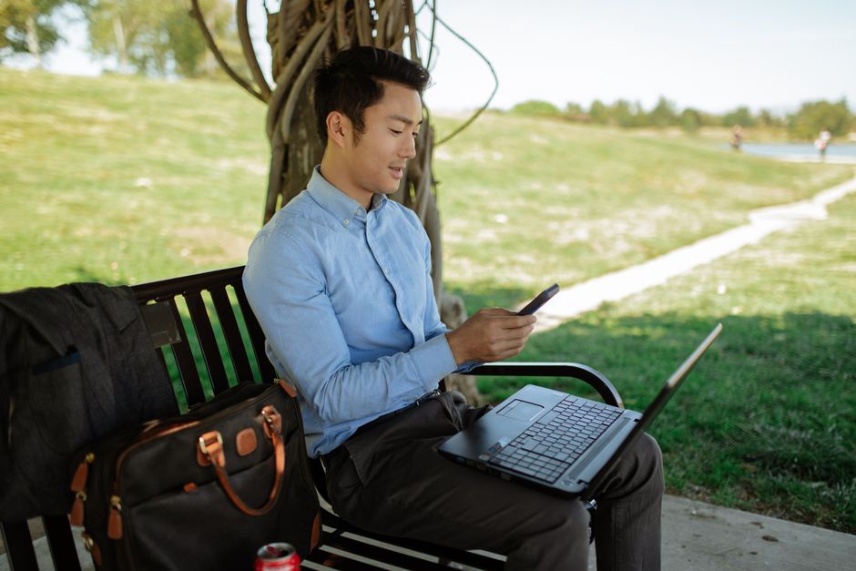 A person efficiently working with a laptop and a smartphone open side-by-side on a desk, illustrating a productive two-device tech setup.