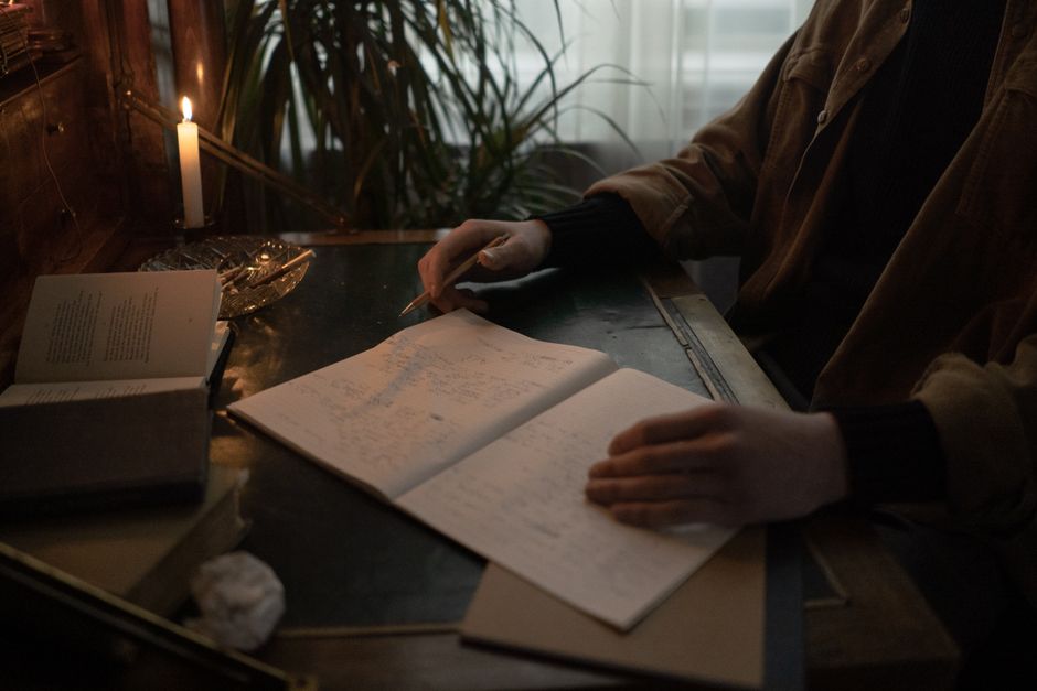 A person wearing noise-cancelling headphones, deeply focused on writing at a tidy desk with a low-profile keyboard and a modern monitor.