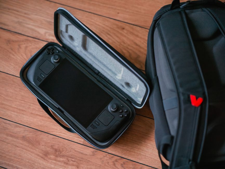 A neatly organized travel kit featuring a handheld gaming console, a power bank, charging cables, a protective case, and noise-canceling headphones, all ready for a trip.
