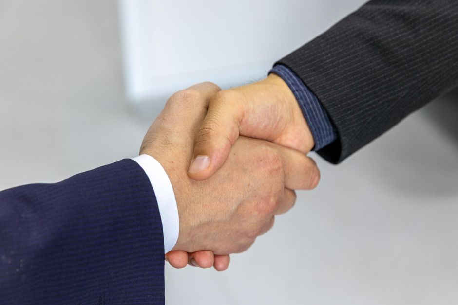 Two professionals, one male and one female, shaking hands in a business setting, but with one person having a subtle, polite expression of refusal or disagreement.