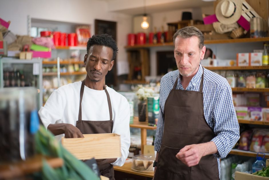 A friendly small business owner smiling and engaging with a customer at the counter of a local coffee shop, with pastries on display.