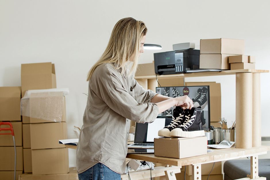 A small business owner happily packaging a product order in branded packaging, surrounded by inventory and shipping labels, representing efficient operations.