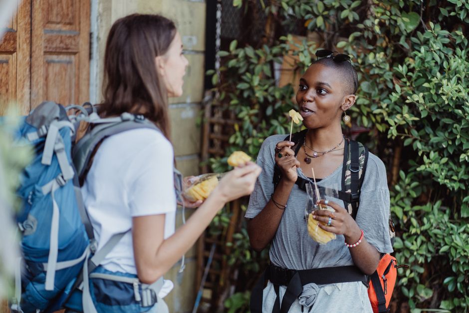 A solo traveler, seen from behind, enjoying a local snack from a street vendor in a lively city square, embodying casual culinary exploration.