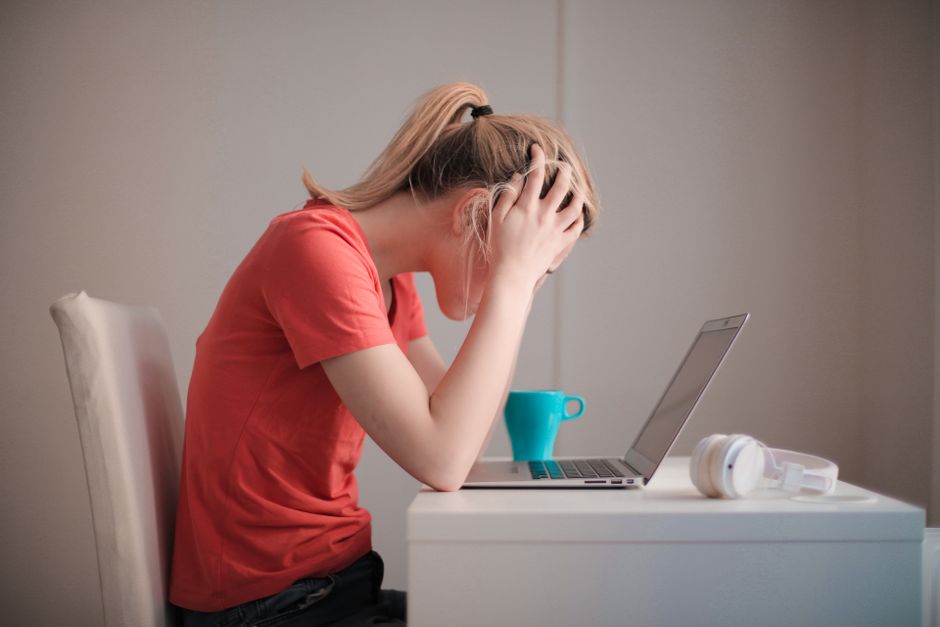 A student with a frustrated expression sitting in front of a laptop showing a large digital game library, hinting at too many unplayed games.