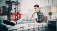 A student relaxing in their dorm room, looking focused while playing a narrative game on their computer.