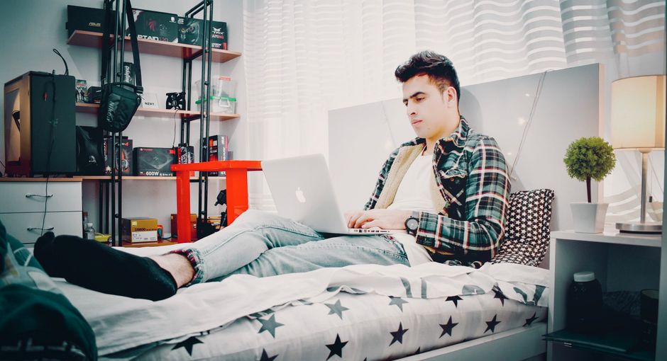 A student relaxing in their dorm room, looking focused while playing a narrative game on their computer.