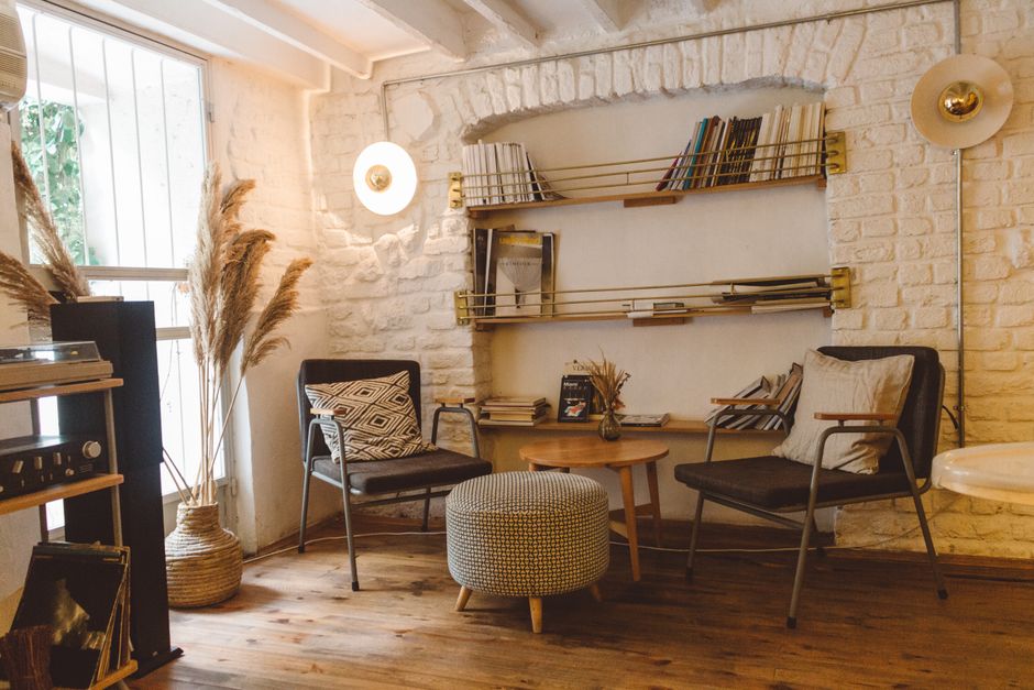 A stylish reading corner in a compact home, featuring a sleek, armless accent chair, a small C-table, and a floating shelf filled with books, demonstrating efficient space utilization.