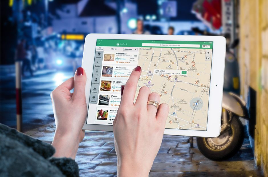 A tablet displaying a travel map, placed next to a passport and coffee cup on a wooden table, symbolizing global travel.