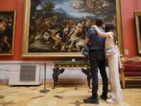 A couple with tired expressions standing in a large, crowded museum gallery, looking overwhelmed by the artworks.