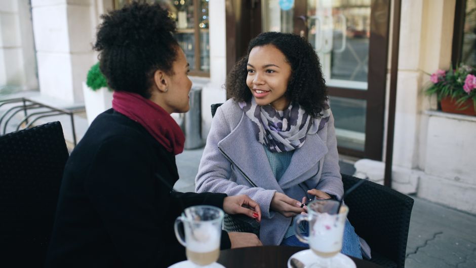 Two individuals engaged in conversation over coffee and pastries inside a lively South American cafe, reflecting local social interaction.